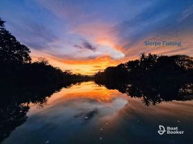 A breathtaking sunset over a tranquil river, reflecting vibrant colors and surrounded by lush greenery — an ideal setting for fishing and nature lovers.