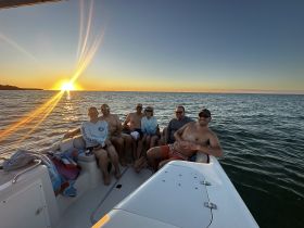 A cheerful group enjoys a sunset cruise on the water, capturing the perfect moment of camaraderie and relaxation as the sun sets on the horizon.