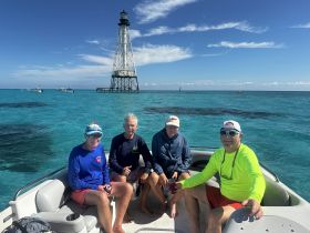A cheerful group of friends enjoys a day on the water near a lighthouse, surrounded by stunning turquoise waters — perfect for memorable boating adventures.