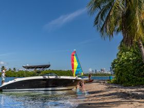 A vibrant beach scene featuring a group enjoying the sun and water activities, with a sailboat and motorboat anchored nearby — perfect for a fun day out on the water.