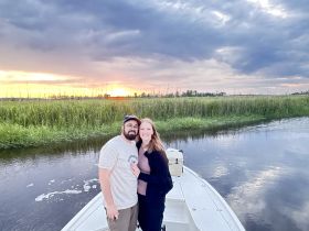 A couple enjoys a romantic moment on a boat at sunset, surrounded by lush greenery — a perfect backdrop for memorable experiences on the water.