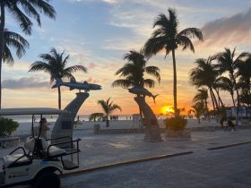 A picturesque sunset view at the beach, framed by palm trees and sculptures, capturing the essence of a tropical getaway.