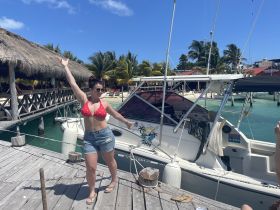 A woman poses joyfully on the dock next to a boat, capturing the essence of a fun tropical vacation. The vibrant setting and her cheerful demeanor highlight the excitement of a day on the water.