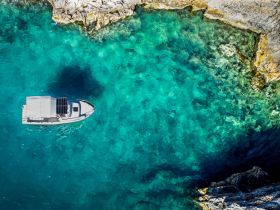 Aerial view of a sleek boat navigating through crystal-clear turquoise waters, showcasing the beauty of the surrounding rocky coastline.