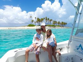A joyful family poses on the deck of a boat with a picturesque island backdrop, perfect for memorable beach adventures and family outings.