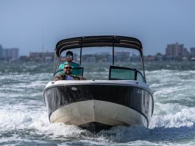 Two friends enjoy a thrilling ride on a speedboat, capturing the excitement of a day on the water with city views in the background.