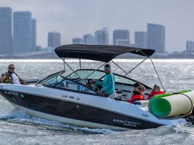 A family enjoys a day on the water aboard a Monterey boat, with kids in life jackets and a fun floating mat in tow — perfect for summer adventures.
