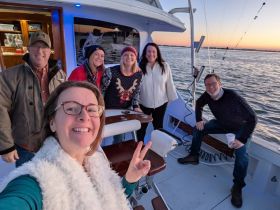 A cheerful group poses for a selfie on a boat during sunset, capturing a memorable moment of celebration on the water.