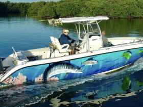 A fishing boat navigates through serene waters surrounded by mangroves, showcasing a vibrant design and two anglers enjoying their time on the water.