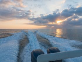 A stunning view from the back of a boat as it cuts through calm waters at sunset, showcasing the beautiful reflections and serene atmosphere of a perfect evening on the water.
