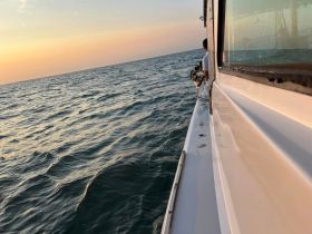 A serene sunset view from a boat, with a person holding a wreath, creating a poignant moment on the water.
