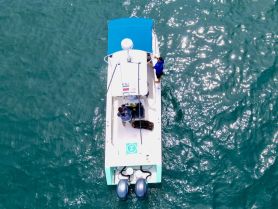 Aerial view of a boat in motion with two individuals onboard, showcasing the vibrant waters and the boating experience.
