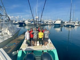 A cheerful group poses on the deck of a fishing boat at the marina, ready for a day of adventure on the water.