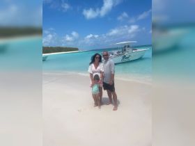 A family enjoys a sunny day at the beach with a boat in the background, capturing a perfect vacation moment in paradise.