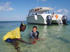 A fun snorkeling experience with a guide and a young swimmer in shallow waters, alongside a catamaran — perfect for family adventures and aquatic exploration.