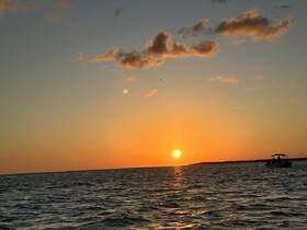 A serene sunset view over the water with a boat silhouetted against the vibrant sky, perfect for capturing the tranquility of evening cruises.