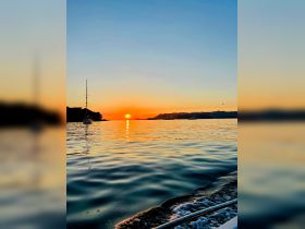 A serene sunset view over calm waters with a yacht silhouetted against the vibrant sky, perfect for capturing the tranquility of evening boat outings.