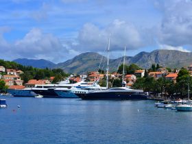 A picturesque view of several luxurious yachts docked in a serene harbor, surrounded by charming coastal architecture and lush mountains, perfect for showcasing the beauty of maritime destinations.
