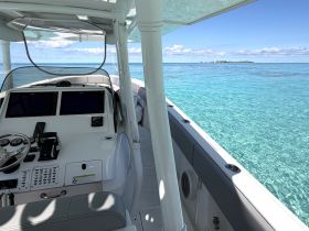 A sleek view of the helm and console inside a modern boat, showcasing advanced navigation equipment against a backdrop of clear turquoise waters.