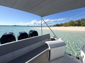 A view of the interior of a boat featuring comfortable seating and a helm, with a picturesque beach and clear waters in the background, perfect for a day of relaxation on the water.