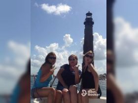 A fun group poses on a boat with a lighthouse in the background, capturing a memorable moment during their boating adventure.