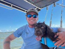 A smiling individual enjoys a day on the water with their dog, showcasing the joy of boating and companionship in the great outdoors.