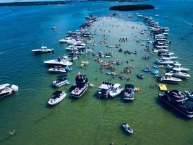 A vibrant scene at a sandbar with numerous boats and groups of people enjoying swimming and sunbathing — a perfect summer party atmosphere on the water.