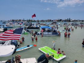 A vibrant scene at a sandbar with numerous boats and people enjoying the water, celebrating summer with swimming and fun activities.