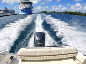 A dynamic view from the back of a speedboat cruising through clear waters, with large cruise ships docked in the background, showcasing a vibrant day on the water.