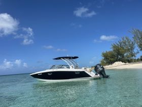 A sleek speedboat anchored in clear turquoise waters, showcasing its elegant design against a backdrop of blue skies and lush greenery.