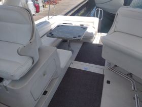 Interior view of a boat's seating area featuring comfortable white upholstery and a central table, ideal for relaxing and dining while on the water.