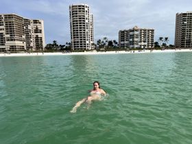 A woman enjoys a refreshing swim in clear waters with beachfront high-rises in the background, capturing the essence of a perfect beach day.