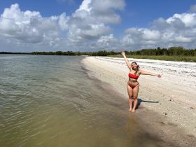 A joyful woman poses on the beach, celebrating a sunny day by the water — perfect for beach outings and fun adventures.