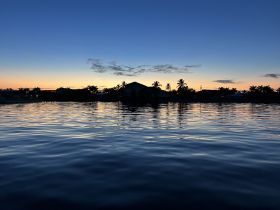 A serene sunset view over calm waters, reflecting the silhouettes of palm trees and buildings — a perfect backdrop for evening boat rides.