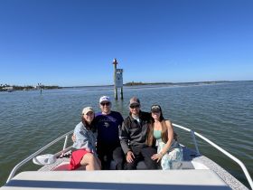 A cheerful group poses on the bow of a boat, enjoying a sunny day on the water near a scenic waterway. Perfect for memorable outings and celebrations.