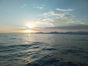 A stunning sunset over the ocean, with mountains in the background, creating a picturesque scene perfect for evening cruises or relaxation on the water.