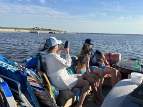 A group enjoys a relaxing day on the water, capturing moments on their phones while snacking aboard a boat — perfect for summer outings and fun with friends.