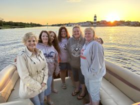 A group of friends poses together on a pontoon boat at sunset, capturing a moment of joy and camaraderie on the water.