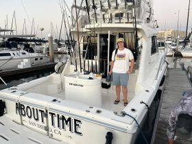 A young man stands on the deck of the 'About Time' fishing boat in San Diego, showcasing the boat's helm and fishing gear — perfect for a day out on the water.