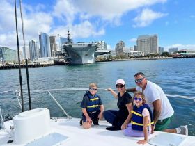 A family enjoys a scenic boat ride with a stunning cityscape in the background, showcasing their adventure on the water while wearing life jackets.