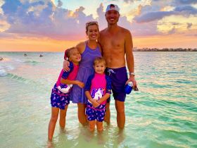 A joyful family poses together in shallow water at sunset, capturing a perfect beach moment filled with love and fun.