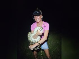 A woman holds a large snake in a nighttime setting, showcasing a unique human-animal interaction that highlights the thrill of wildlife encounters.