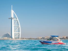 A vibrant boat glides through the turquoise waters of Dubai, with the iconic Burj Al Arab in the background, showcasing the perfect blend of luxury and adventure on the water.