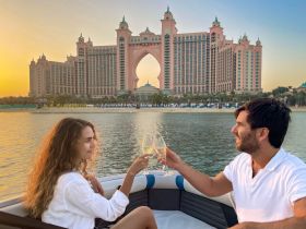 A couple toasts with cocktails on a boat at sunset, with the stunning Atlantis hotel in the background — a perfect romantic getaway on the water.
