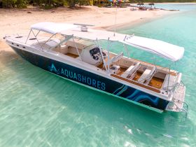 An aerial view of a sleek speedboat named 'Aquashores' docked in clear turquoise waters, perfect for a day of adventure on the sea.