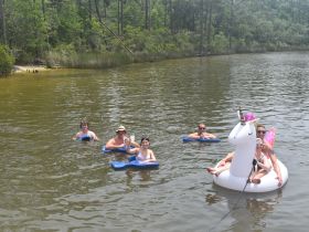 A lively group enjoys a summer day swimming in the water, featuring a fun unicorn float and drinks — perfect for a memorable day out with friends.
