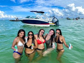 A lively group of friends enjoys a fun day in the water, holding drinks and celebrating near their boat — perfect for summer outings and beach parties.