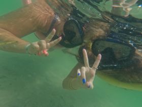 Two friends enjoy snorkeling underwater, flashing peace signs in the crystal-clear water — a perfect moment of fun and adventure on their aquatic journey.