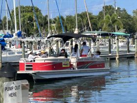 A lively group enjoys a day on a pontoon boat at the marina, surrounded by sailboats and palm trees — perfect for family outings or group adventures on the water.