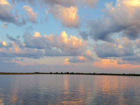 A serene view of clouds reflecting on calm waters, creating a picturesque sunset scene.